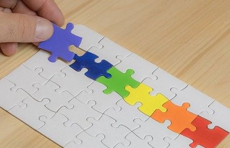 eine Hand, die regenbogenfarbene Puzzleteile in ein weißes Puzzle einfügt