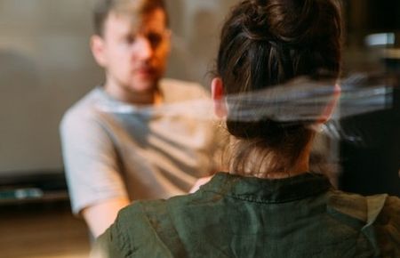 Frau sitzt mit dem Rücken zum Betrachter im Gespräch mit einem Mann am Tisch