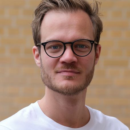 junger, blonder Mann mit leichten Bart, Brille und weißem Shirt