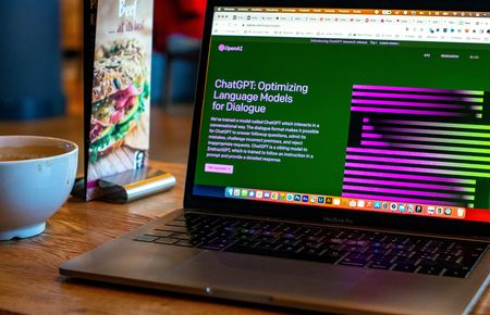 Laptop mit ChatGPT auf dem Screen, daneben ein Flyer und ein eine Tasse