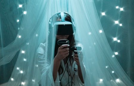 Frau in bläulichem Raum unter Moskitonetz mit virtueller Brille