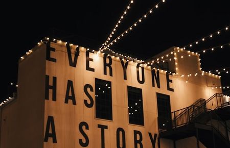 Häuserwand bei Nacht mit Lichterketten und der Aufschrift: Everyone has a story
