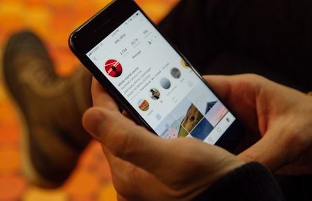 Handyscreen mit Instagram gehalten von einer männlichen Hand vor orangenem Hintergrund