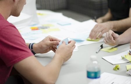 Menschen sitzen am Arbeitstisch in einem kreativen Prozess mit Papier, Post-its, Stiften etc.