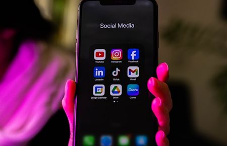 Frauenhand hält Handy mit Social Media Icons, rötliches Licht