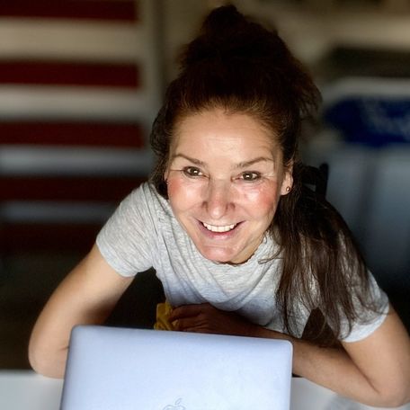von schräg oben fotografiert, eine brünette, lächelnde Frau mit sympatischer Ausstrahlung vor einem Laptop sitzend