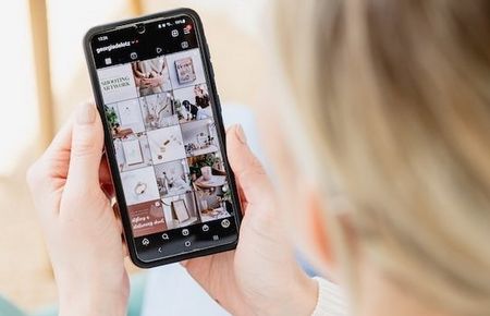 Hinterkopf Frau, die ein Handy, was sie in den Händen hält, mit geöffnetem Insta-Account ansieht