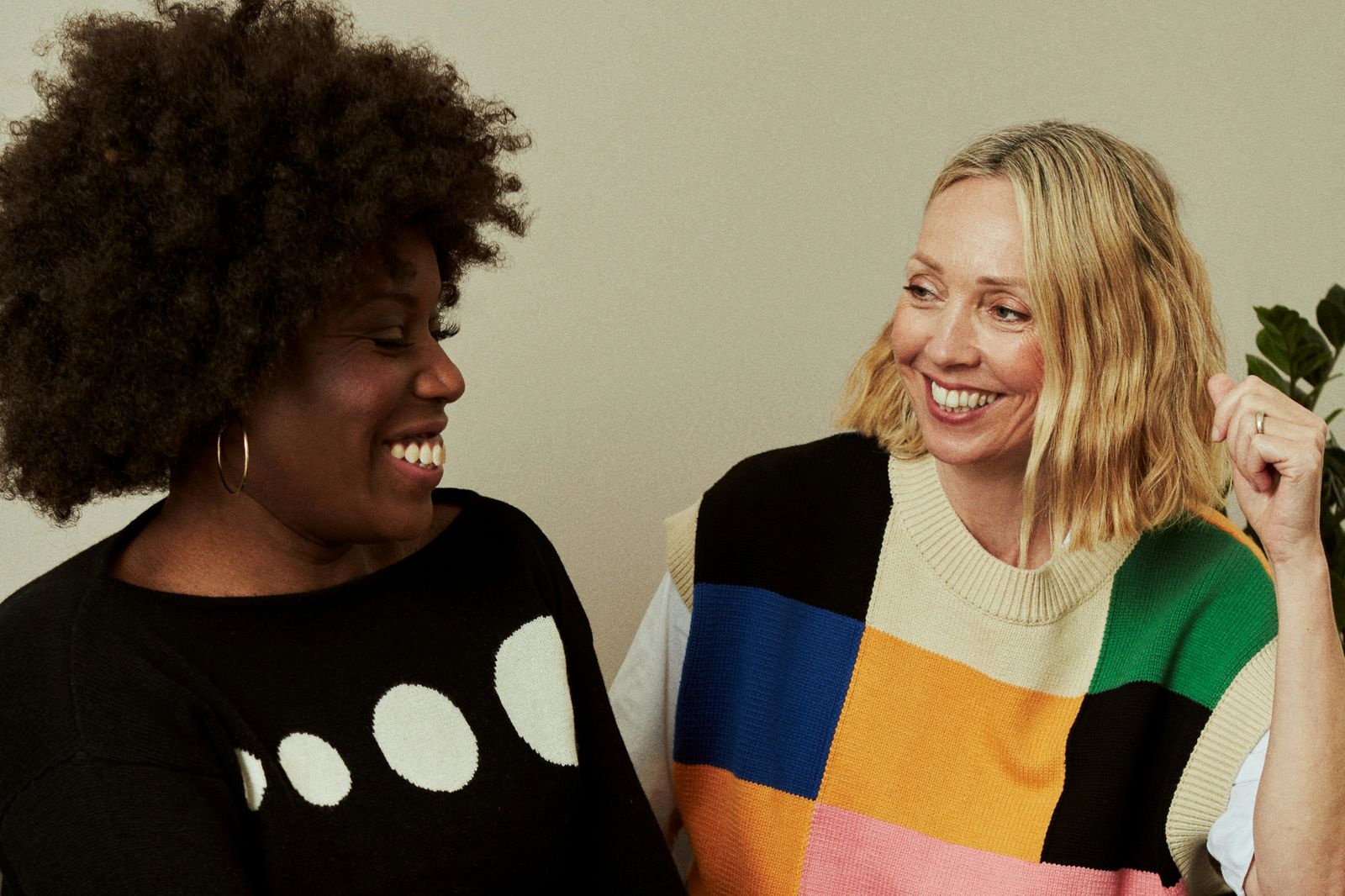zwei Frauen unterschiedlicher Hautfarbe sitzen zugewandt nebeneinander lachen
