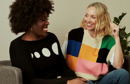 zwei Frauen unterschiedlicher Hautfarbe sitzen zugewandt nebeneinander lachen