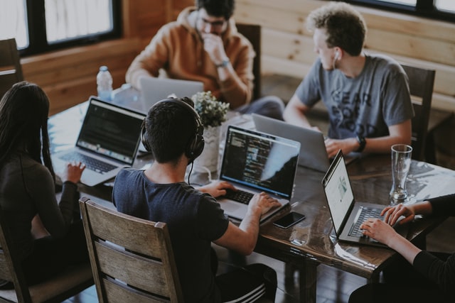 Eine Gruppe junger Erwachsener sitzt an einem Tisch vor ihren Laptops.