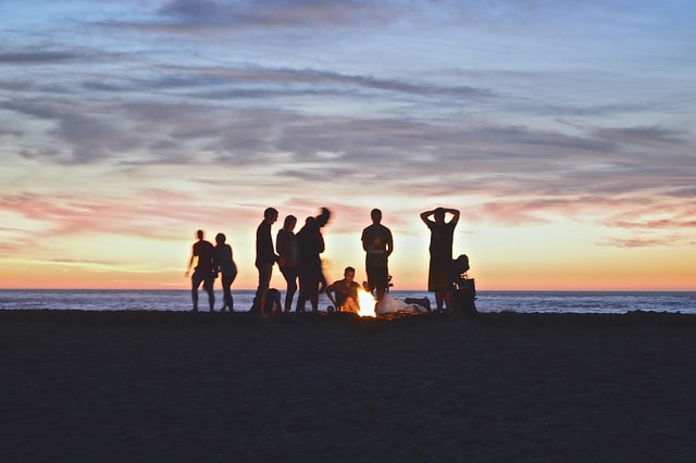 Menschen stehen um ein Lagerfeuer in der Abendsonne